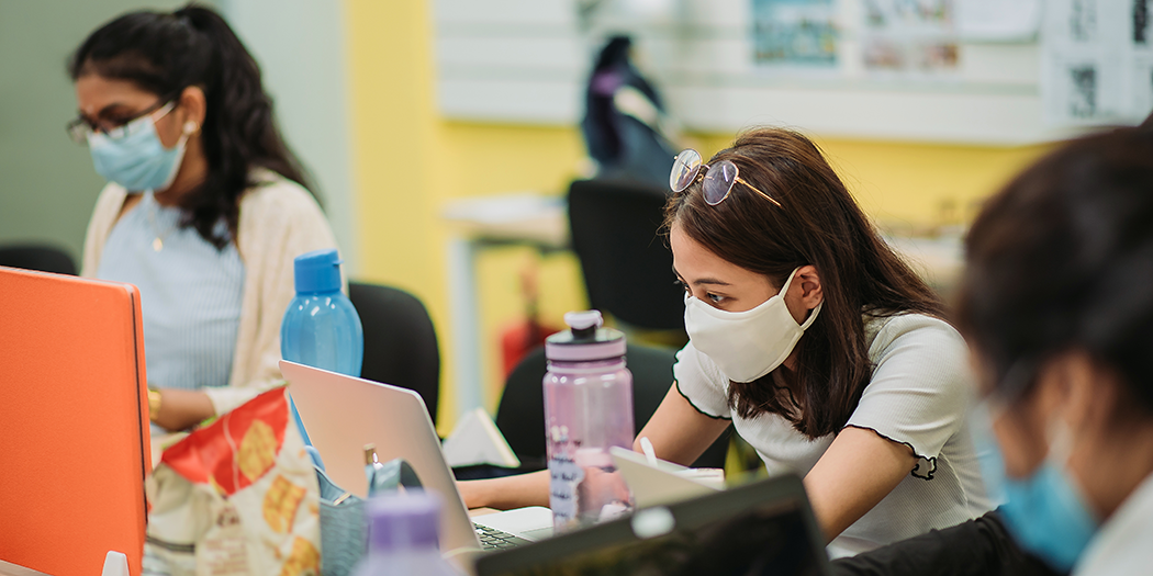 Community college students wearing masks work on computers 