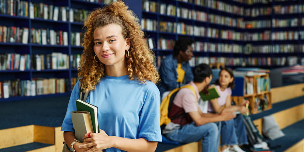 A smiling girl holding books in a library.