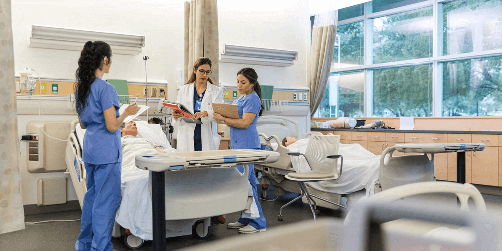 Photo of health care students around a hospital bed holding a medical mannequin.